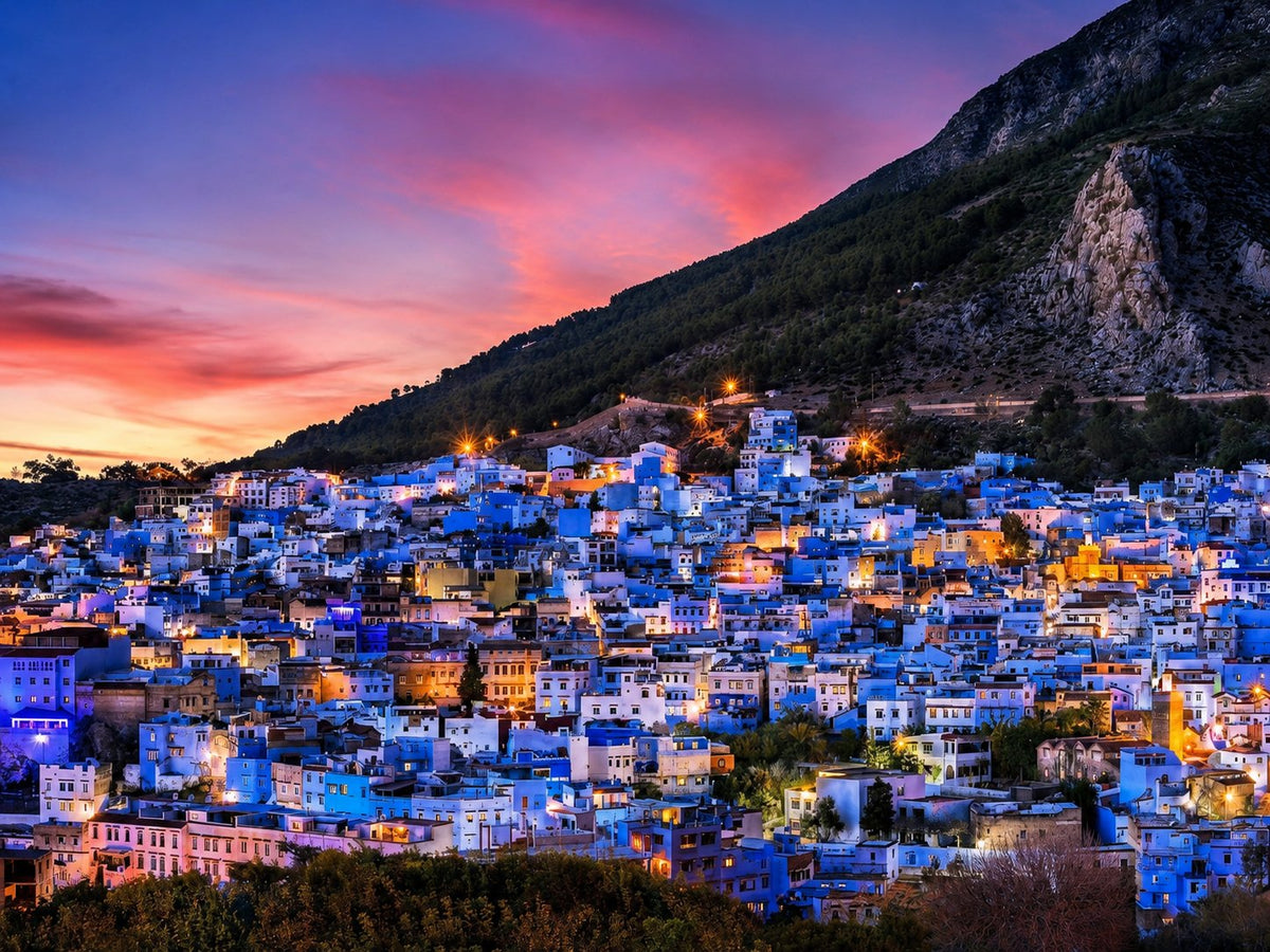 Blue houses of Chefchaouen on a hillside at dusk under a pink sky
