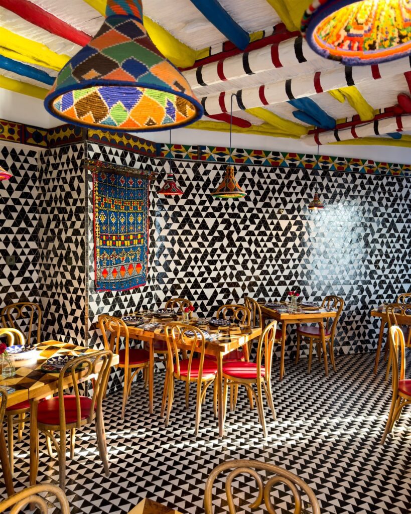 Restaurant with black-and-white patterned tiles, wooden chairs and painted beams with hanging lanterns