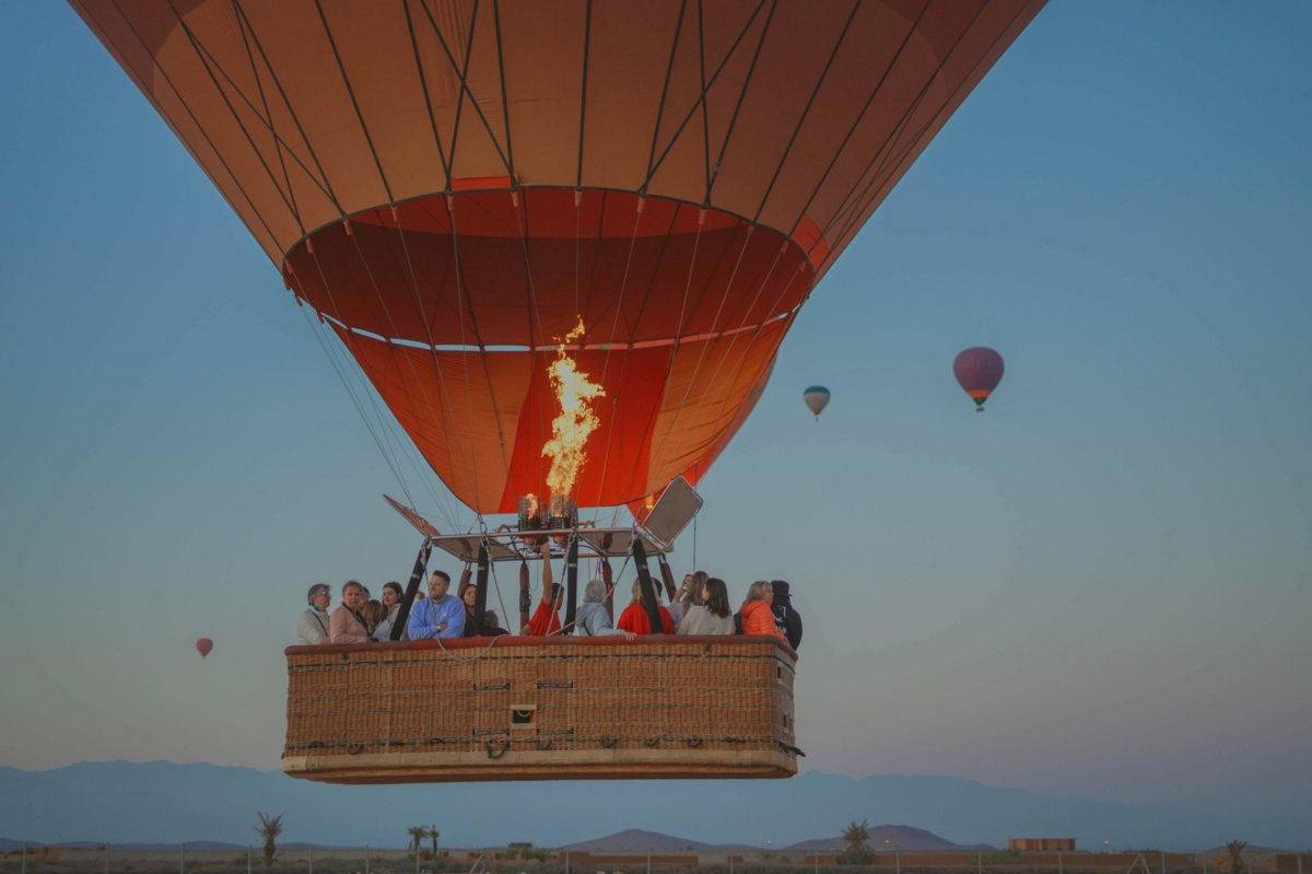 Hot-air balloon basket full of passengers rising with the burner lit, two balloons in the distance