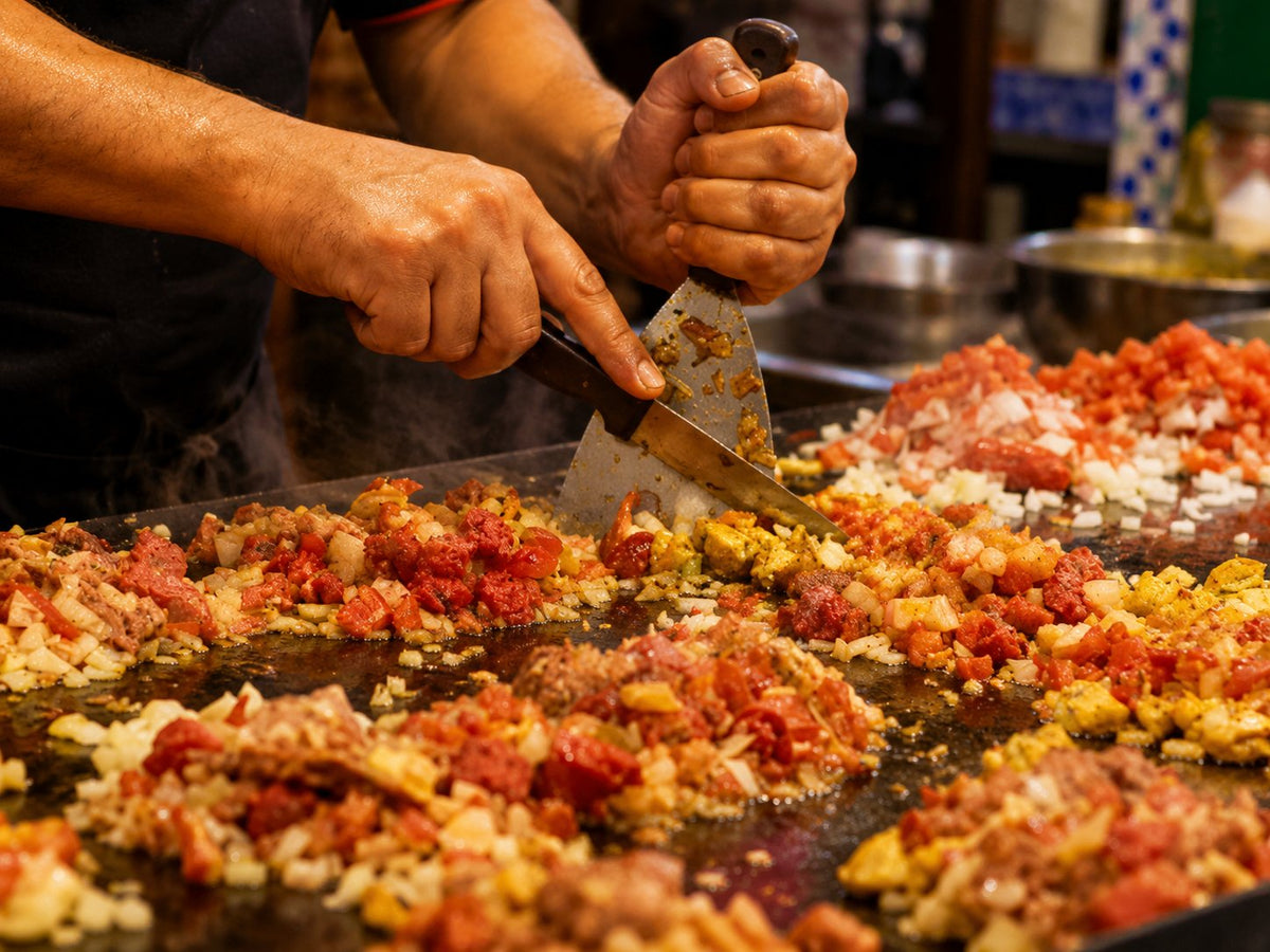Cook chopping minced meat and vegetables with a spatula on a hot griddle
