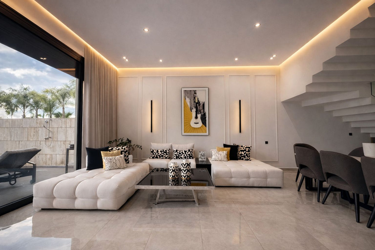 A bright living room with white sofas beside a floating staircase
