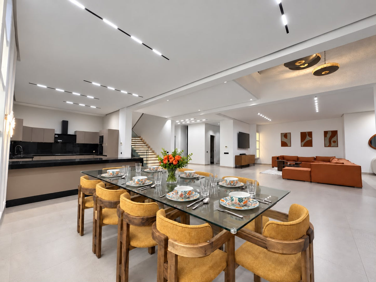 A dining table with wooden chairs and the open kitchen behind