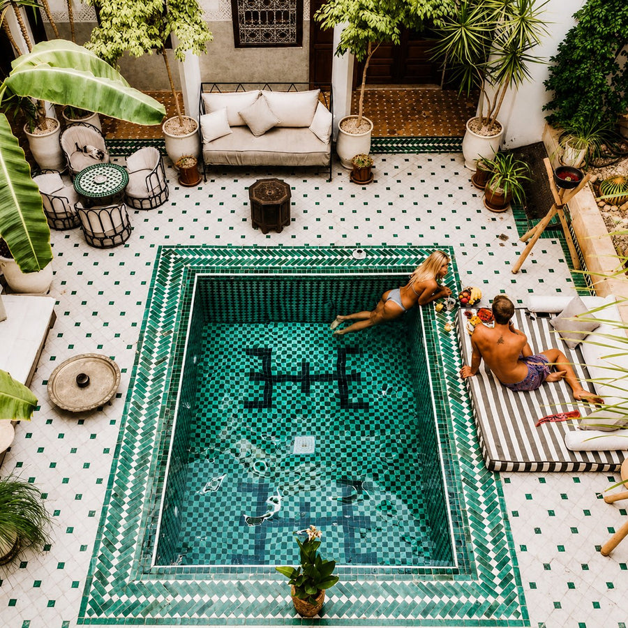 Couple lounging beside a green-tiled riad plunge pool seen from above, plants and low tables around