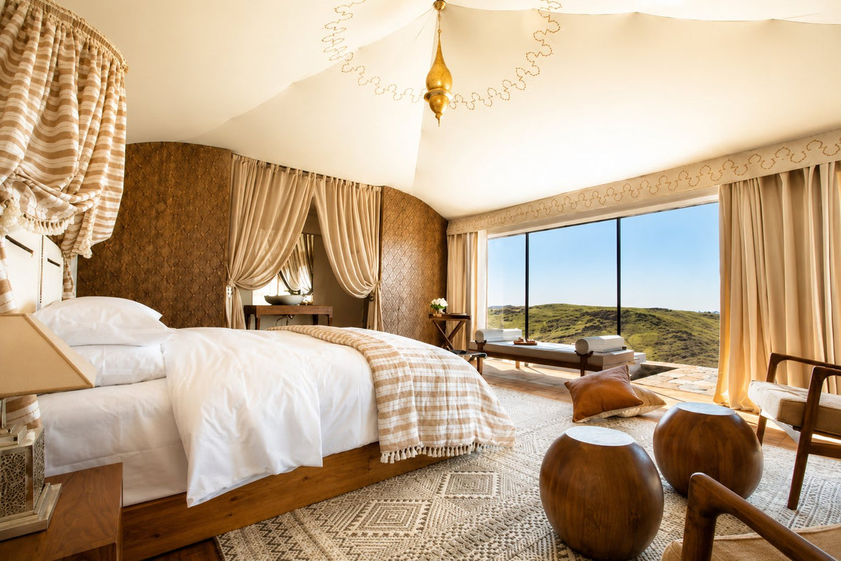 Tented bedroom with a white bed, draped curtains and a view over rolling hills
