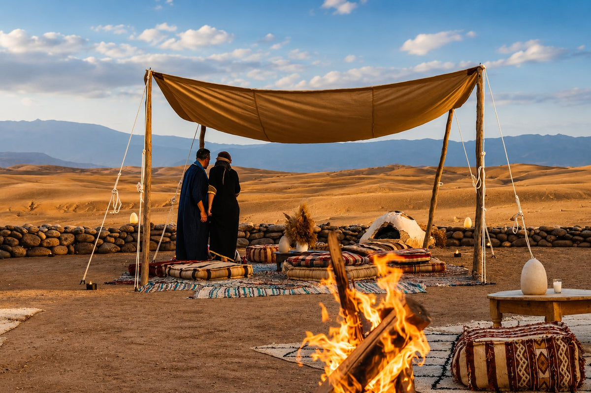Couple under a canvas canopy beside a fire pit with cushions and rugs, hills behind