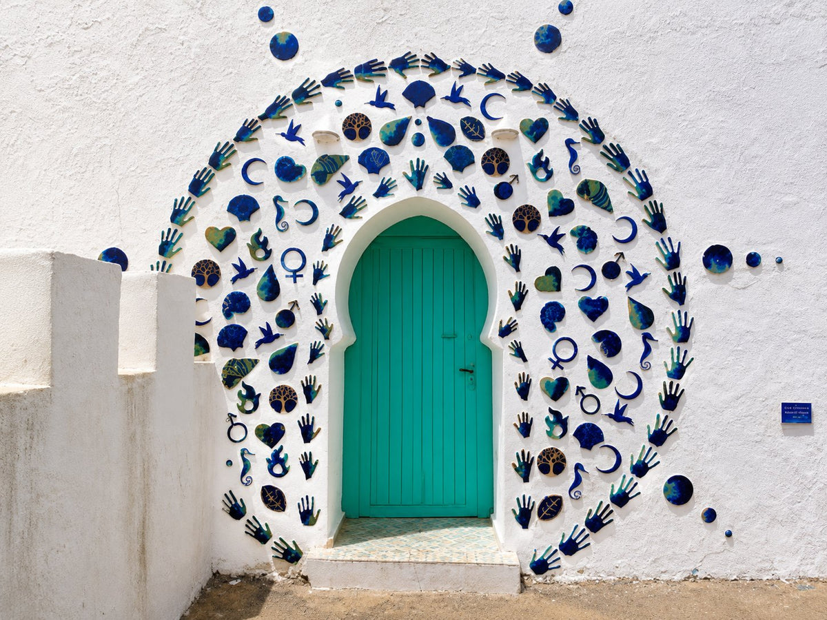 Turquoise arched door in a white wall decorated with painted hands and shells