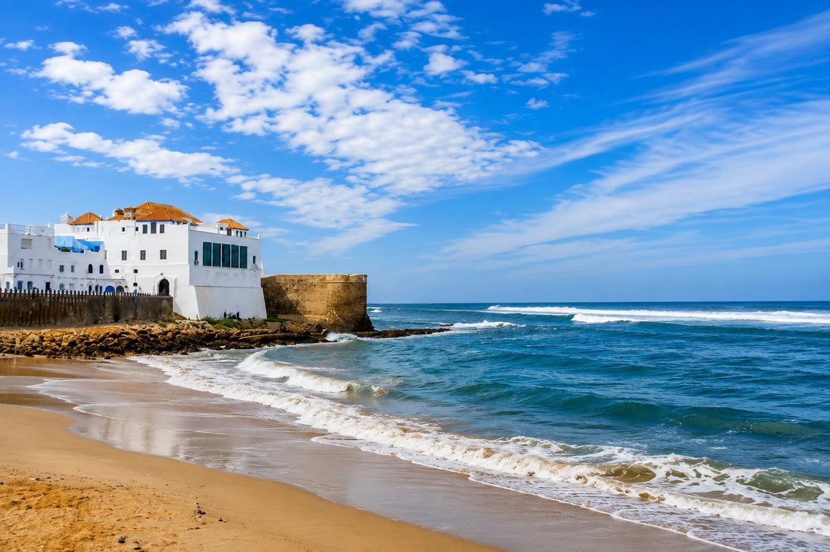 Sandy beach and waves below the white ramparts of Asilah under a blue sky