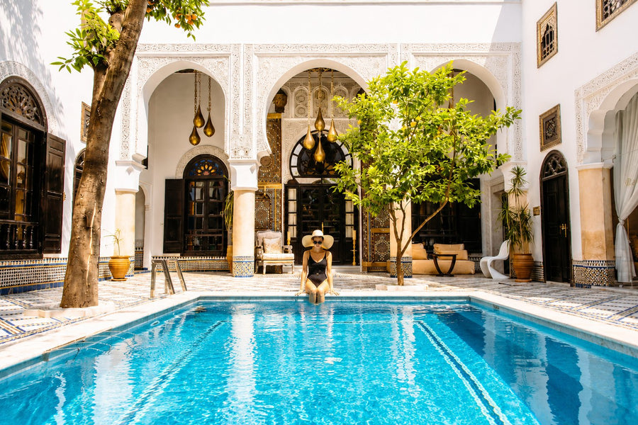 A studded cedar door half-open onto a narrow Marrakech medina lane revealing a sunlit courtyard, Morocco.