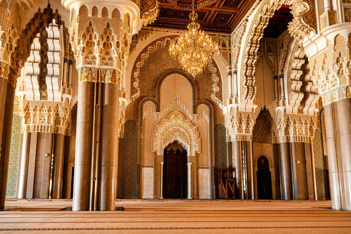 Carved plaster arches and marble columns inside the Hassan II Mosque, chandelier above