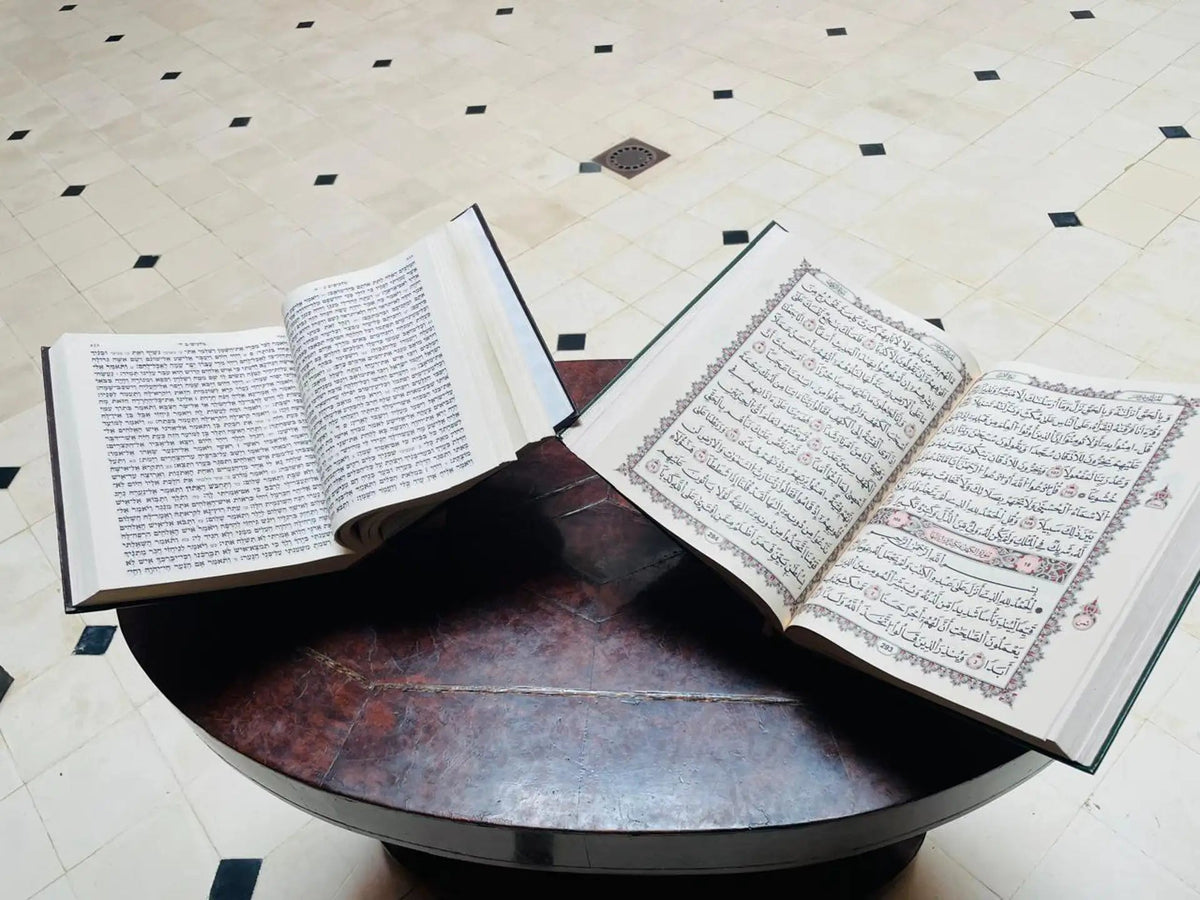 Two open books of Arabic script on a round dark table on a tiled floor