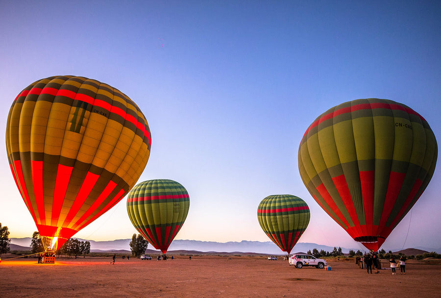 Four striped hot-air balloons inflating at dawn on flat ground, cars and people nearby