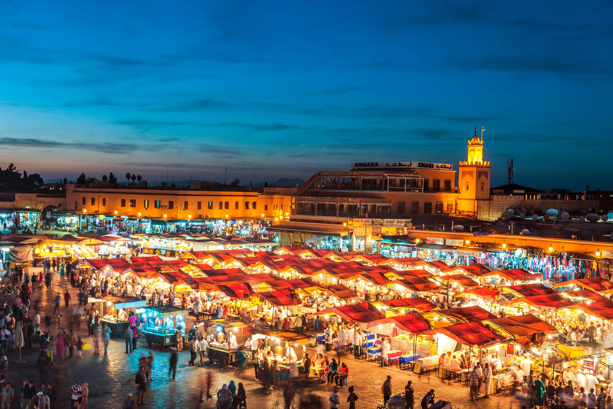 Jemaa el-Fna square at dusk, lit food stalls and a minaret in the background