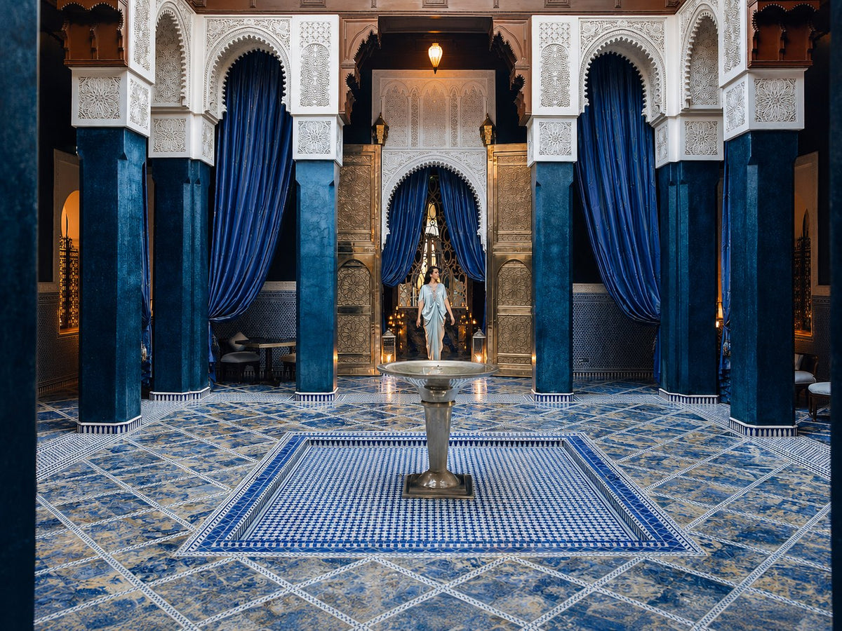 Blue-tiled courtyard with a central fountain between dark columns and white carved arches