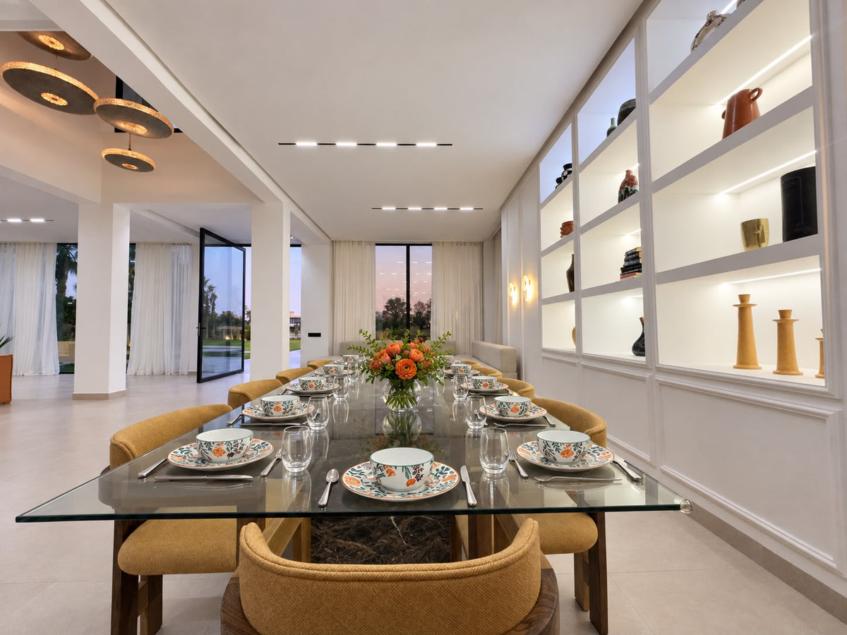 A long glass dining table laid for dinner in a bright villa living room