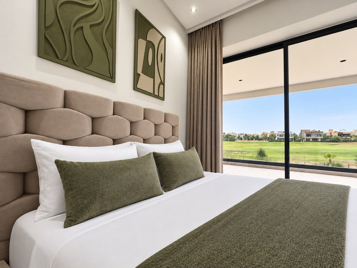 A bedroom with an upholstered headboard, green linen and a view of open fields