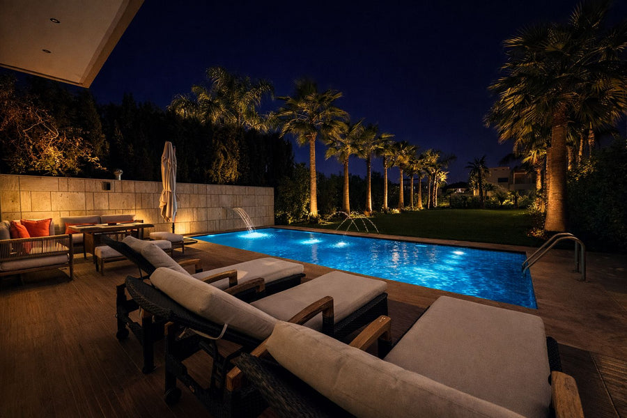 The pool and terrace of a private villa lit at night, palm trees behind