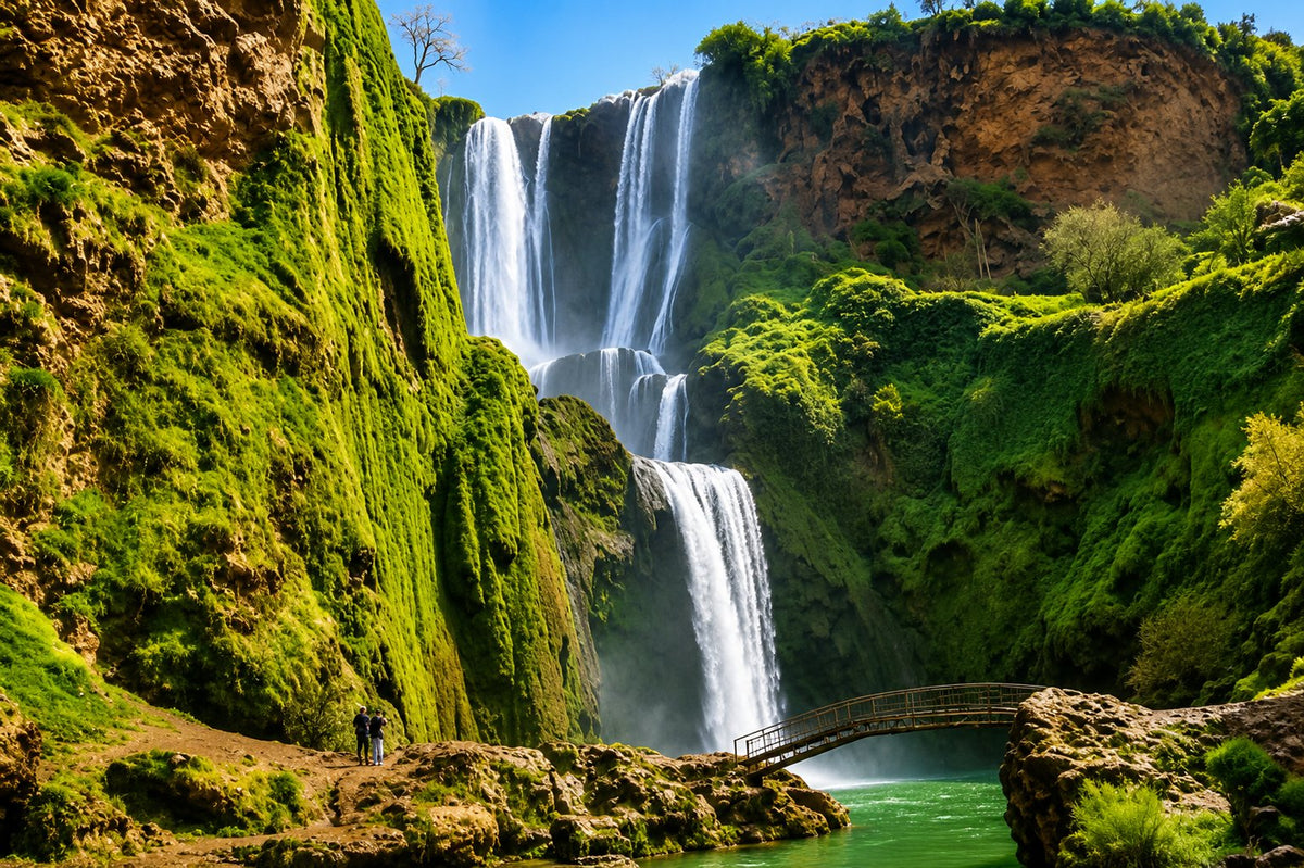 Ouzoud waterfalls cascading down moss-covered cliffs, a small bridge over the pool below