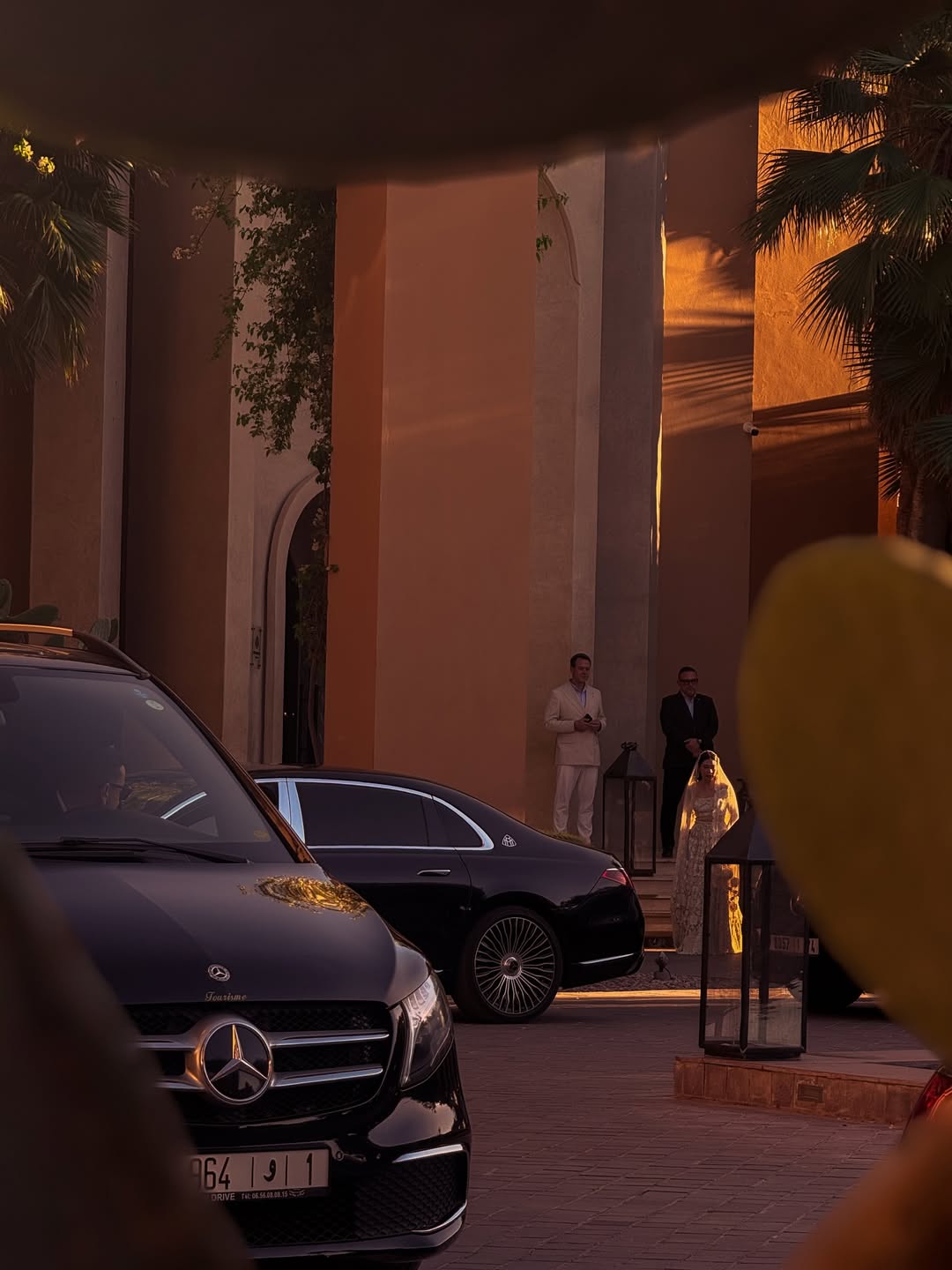 Black Mercedes sedan waiting at a hotel entrance at dusk, doorman at the door