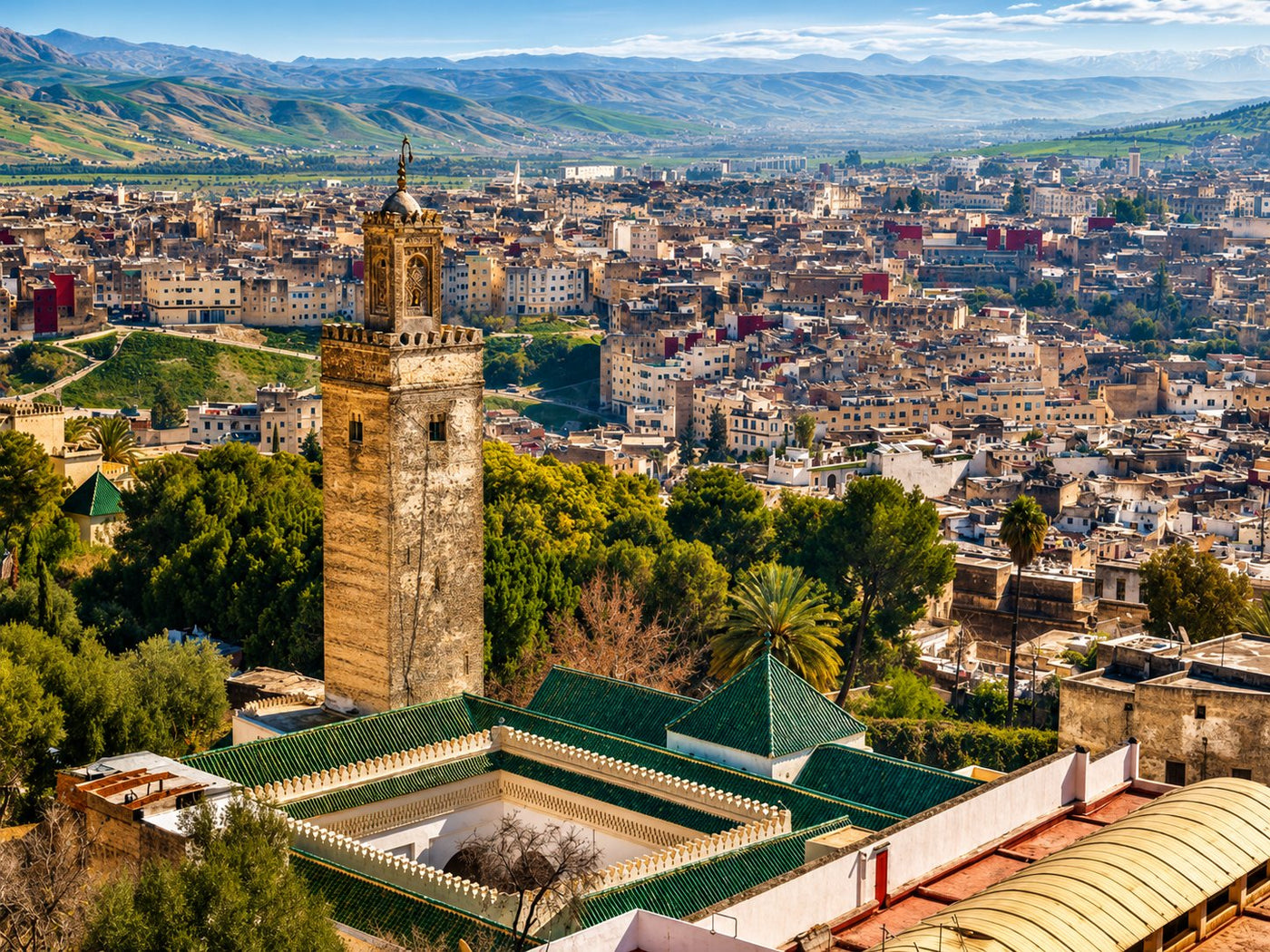 Rooftops and green-tiled minaret of a medina seen from above, hills in the distance