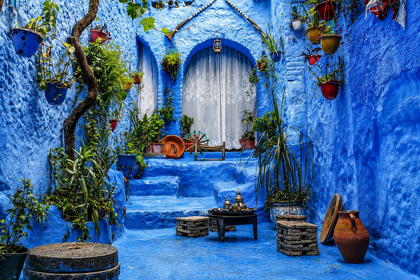Blue-washed alley with potted plants on the steps and a curtained doorway