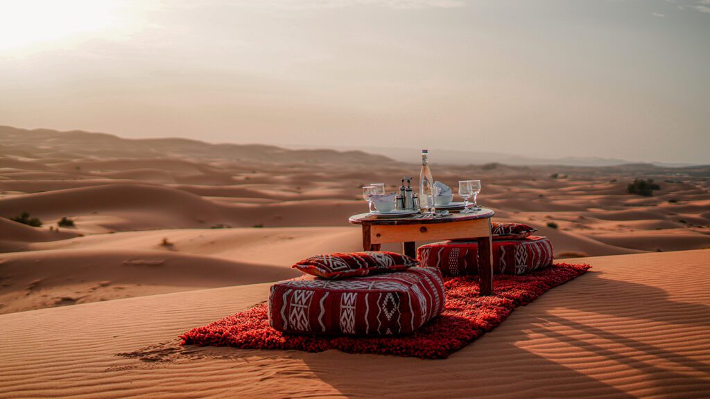 Low table with red Berber rugs and cushions set on sand dunes in late afternoon light